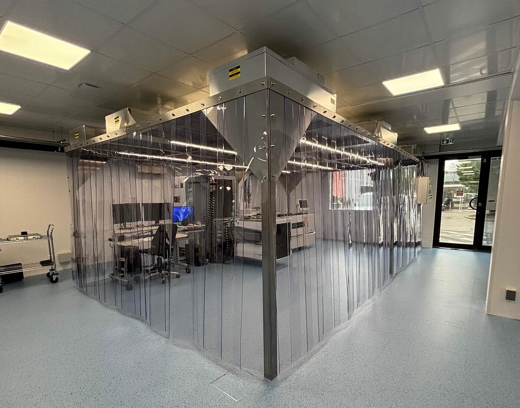 Clean laboratory with a clear plastic curtain enclosure around a central workstation and equipment inside a bright room.