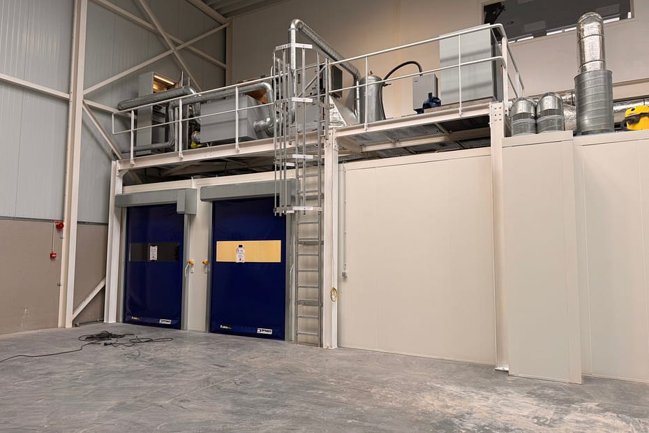Industrial service area with metal catwalk, blue doors, and large ductwork running along the ceiling.